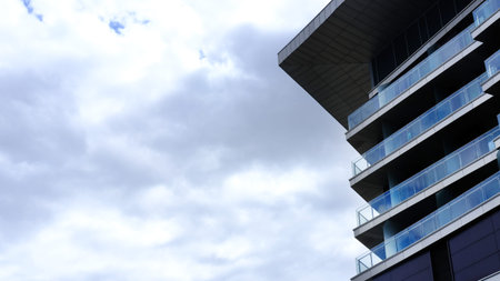 Contemporary building features glass balconies and a bold overhang, surrounded by a moody sky, highlighting innovative architecture and urban lifestyleの写真素材