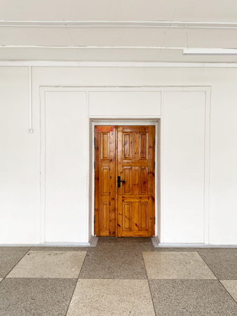 Wooden door set within white walls and a tiled floor, creating a minimalist aesthetic with natural light highlighting the entranceの写真素材