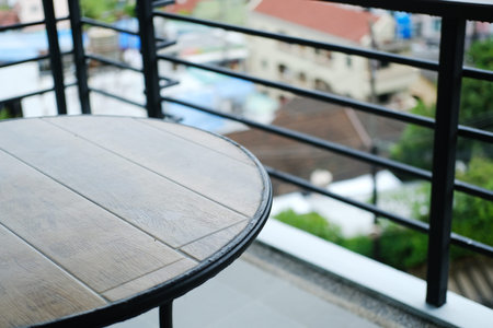 Wooden round table positioned on a balcony overlooking rooftops and greenery, with a modern railing...