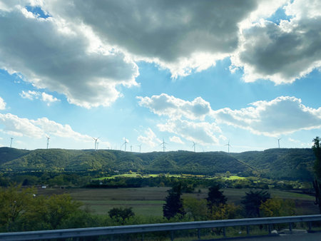 Rolling hills with wind turbines are visible under a partly cloudy sky, seen from a bus window while...