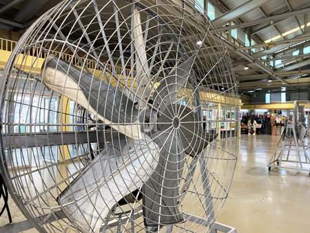 Large industrial fan with metal blades and protective grille located in a shopping center,...