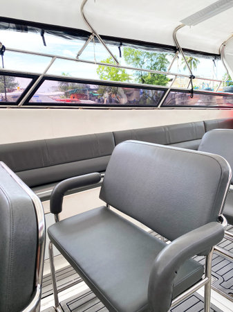 Empty gray cushioned seats on a tourist boat, featuring large windows that allow natural light and views of the outside environmentの写真素材