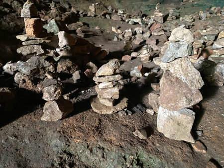 Stone cairns of different sizes are positioned on the cave floor, surrounded by scattered rocks and...