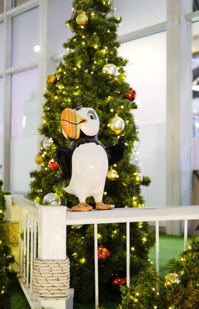 Whimsical bird sculpture stands beside a decorated Christmas tree, surrounded by twinkling lights and colorful ornaments, enhancing the festive mood in a public areaの写真素材