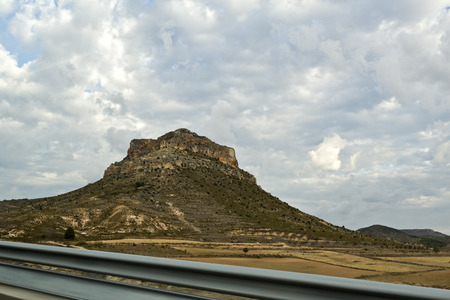 Mesa in the arid central Spain country seen from the highway. Mesas are elevated areas of land with a flat top and sides that are usually steep cliffs formed by weathering and erosion of horizontally layered rocks.の写真素材