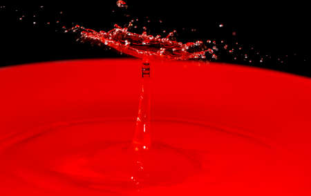 Un umbrella shape resulting from a drop collision above a red water pool and a black backgroundの写真素材