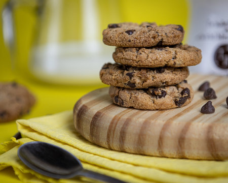 wooden board with cookies and chocolate chips in close-up on yellow background.