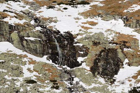 Waterfall in the winter mountains with texture of snow and rockの写真素材