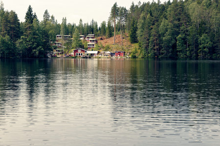Settlement in Finland on the shore of the lake with classic red wooden buildings vibrant to the green forestの写真素材