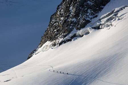 Groups of mountaineers crossing a glacier with crevasses on the sunriseの写真素材