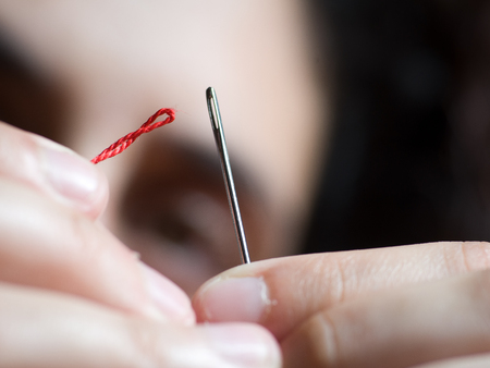 Woman trying to thread a needle with a red threadの写真素材
