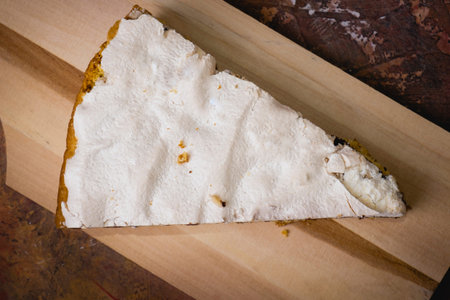 Slice of chocolate cake with meringues on the surface placed on a wooden cutting board