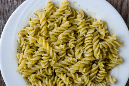 Plate of fusilli pasta with pesto sauce on a wooden table の写真素材