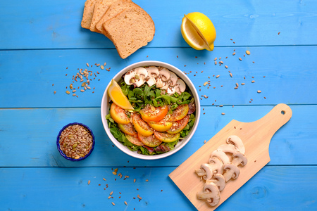 Top view of a bowl of mixed salad with tomatoes, mushrooms, lettuce and seeds with bread on a wooden tableの写真素材