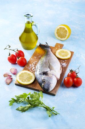 Freshly caught and cleaned sea bream ready to be cooked together with tomatoes, garlic, oil and parsleyの写真素材