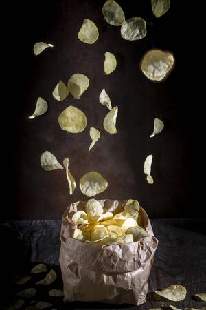 Potato chips fall into a paper bag on a dark rustic backgroundの写真素材