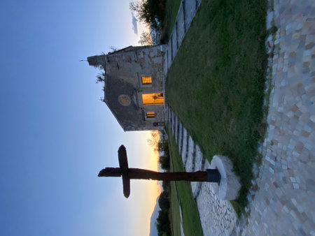 Low angle view of a wooden cross in the foreground with a small church illuminated from inside at sunset in the Abruzzo region, Italyの写真素材
