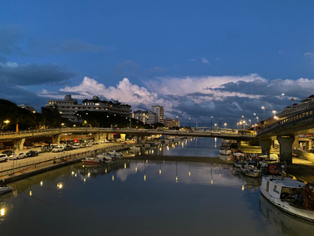 City lights reflecting in the calm waters of the Pescara River at blue hour, with the Ponte Risorgimento bridge and dramatic clouds in the background, Pescara, Abruzzo, Italyの写真素材