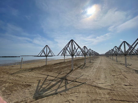 Beach umbrellas casting long shadows, forming geometric patterns across sandy shoreline near Pescara, highlighting linear coastal landscapeの写真素材