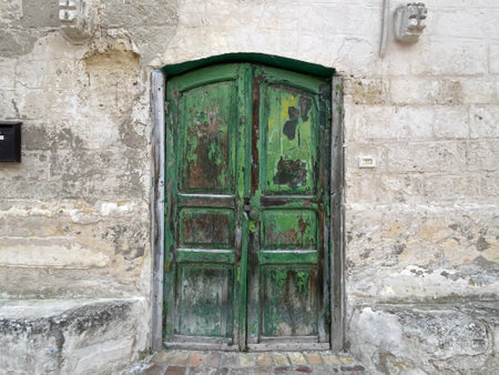 Green wooden door weathering historic stone facade in Matera, Basilicata, capturing rustic architectural charm of southern Italian landscapeの写真素材