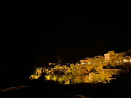Pitigliano medieval village perched on volcanic cliff, glowing under nighttime illumination, revealing enchanting Tuscan architectural silhouettesの写真素材