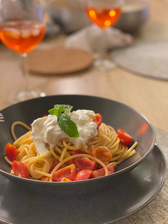 Tasty spaghetti with stracciatella cheese, cherry tomatoes and basil served in a black bowlの写真素材
