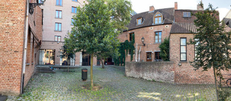 Narrow cobblestone alley winding between historic brick buildings, verdant trees framing traditional Belgian architectural heritage in Mechelenの写真素材