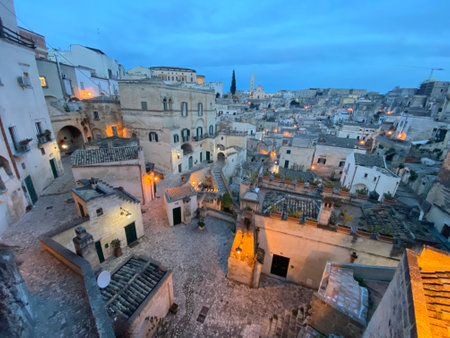Capturing the enchanting evening ambiance of Matera, Italy, with its ancient stone buildings and winding streets illuminated by warm lightsの写真素材