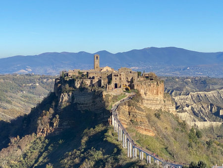 Civita di Bagnoregio, a picturesque hilltop town in Italy, accessible by a long pedestrian bridge, dominates a landscape of valleys and mountainsの写真素材