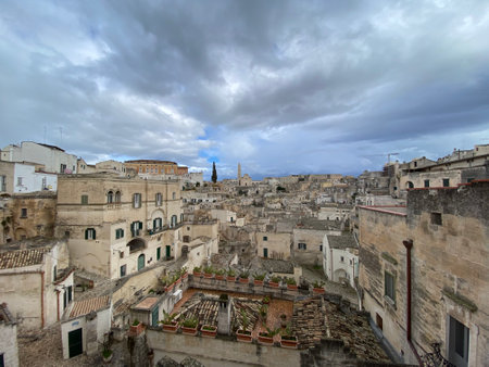Panoramic landscape revealing limestone cave dwellings nestled across Sassi di Matera's historic terrain, showcasing dramatic architectural heritage under overcast southern Italian skiesの写真素材