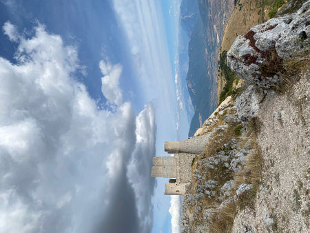 Rocca Calascio castle perching atop rocky outcrop, casting dramatic shadow across cloudy landscape in Abruzzo mountain region, Italyの写真素材