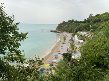 Sunbathing tourists enjoying crystal-clear waters at Ripari di Giobbe beach, nestled among verdant coastal landscape in Ortona, Italyの写真素材