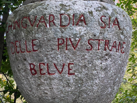 Historic stone with red lettering nestled among verdant foliage in Bomarzo Park, capturing architectural detail and natural landscapeの写真素材