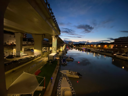 Ponte del Mare and Pescara cityscape reflecting on the canal at twilight, with boats moored along the banks and a highway overpass in the foreground in Pescara, Abruzzo, Italyの写真素材