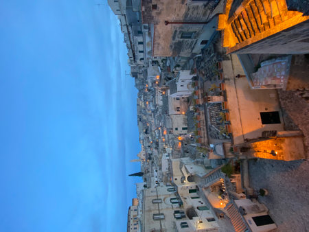 Warm illumination casting golden glow over ancient Sassi di Matera stone dwellings during twilight, revealing historic Basilicata landscape under soft blue skyの写真素材