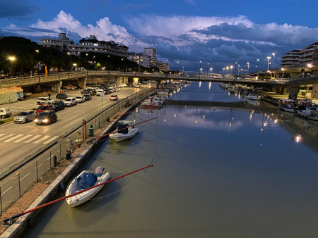 Boats moored along the Pescara River with the cityscape reflecting on the water surface at blue hour in Pescara, Abruzzo, Italyの写真素材