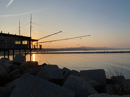 Wooden fishing pier stretching into tranquil Adriatic waters during golden sunset lighting along Pescara coastlineの写真素材