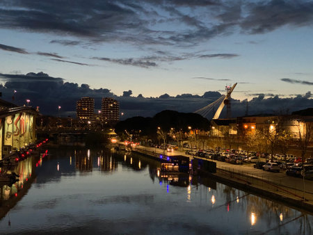 Scenic evening view of Ponte Risorgimento with illuminated buildings reflecting on the calm river under a dramatic skyの写真素材