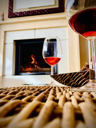 Wine glasses sitting on wicker surface near crackling fireplace inside rustic Italian home in Pineto regional settingの写真素材