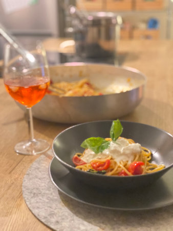 Delicious Italian pasta with burrata cheese, tomatoes and basil, served with a refreshing spritz aperitif in a cozy kitchen in Pineto, Abruzzo, Italy, perfect for a summer eveningの写真素材