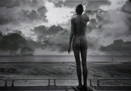 Bronze statue gazing out at the sea beneath a dramatic, cloudy sky, captured in a striking black and white image that evokes solitudeの写真素材