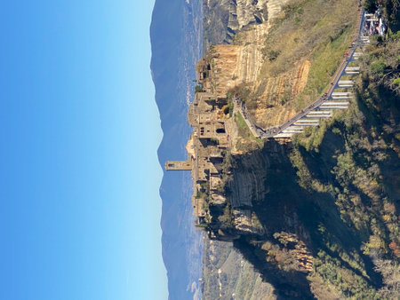 Civita di Bagnoregio, a picturesque hilltop town in Italy, accessible by a long pedestrian bridge, stands majestically on a plateau, offering stunning views of the surrounding landscapeの写真素材