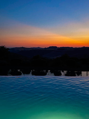Colorful sunset reflecting on the calm water of a swimming pool in the Tuscan countryside, creating...