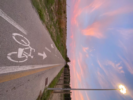 Deserted bike path extending through sunset-lit landscape, white directional markers guiding journey across Pineto's tranquil Abruzzo terrainの写真素材