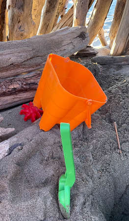 children's beach toys seen up close inside a hut made from wood found on the winter beach. orange bucket, green shovel and red crab mold. rectangular format.の写真素材