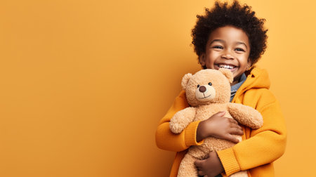 Cheerful african american boy holding teddy bear and smiling at camera isolated on yellowの素材