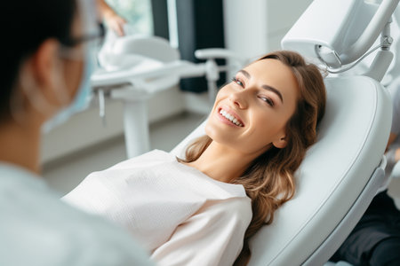 smiling young woman looking at camera while sitting in dental chair in clinicの素材