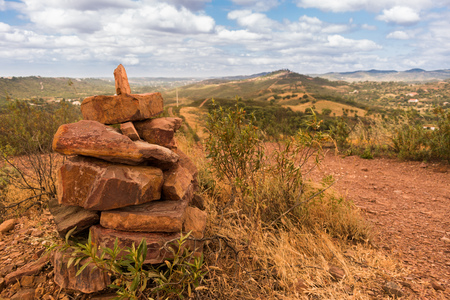 Cairn built on top of a hill under a cloudy sky next to a footpath with a view into the distance in the Silves region countryside in the Algarve, Portugal.の写真素材