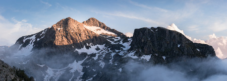 Panorama of Pic Negre de Joclar at sunset taken from near the Refuge de Rulhe on the GR10 hiking route. The snow scattered mountain is caught in the light with nearby mountains and clouds in shadow.の写真素材