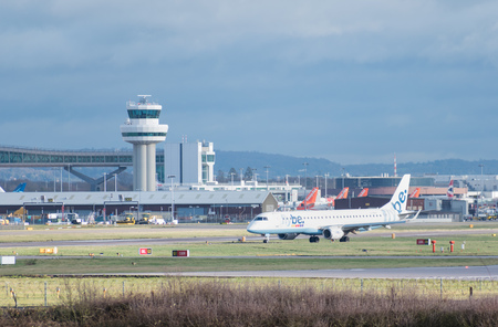 GATWICK AIRPORT, ENGLAND, UK â DECEMBER 09 2018: A Flybe Embraer E190 plane taxis after landing at London Gatwick Airport, with the air traffic control tower in the background. Copy space.のeditorial素材